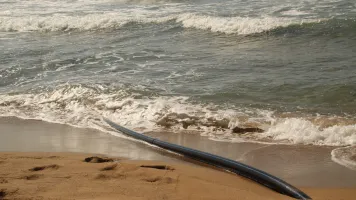 A beach with a black cable that appears from the sand and disappears into the water.